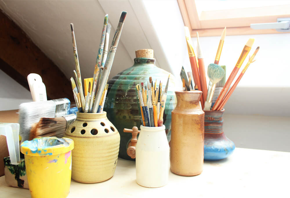 Paintbrushes organized in clay pots and simple containers